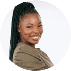 Smiling woman with long braided hair in a ponytail, wearing a brown top, against a white background.